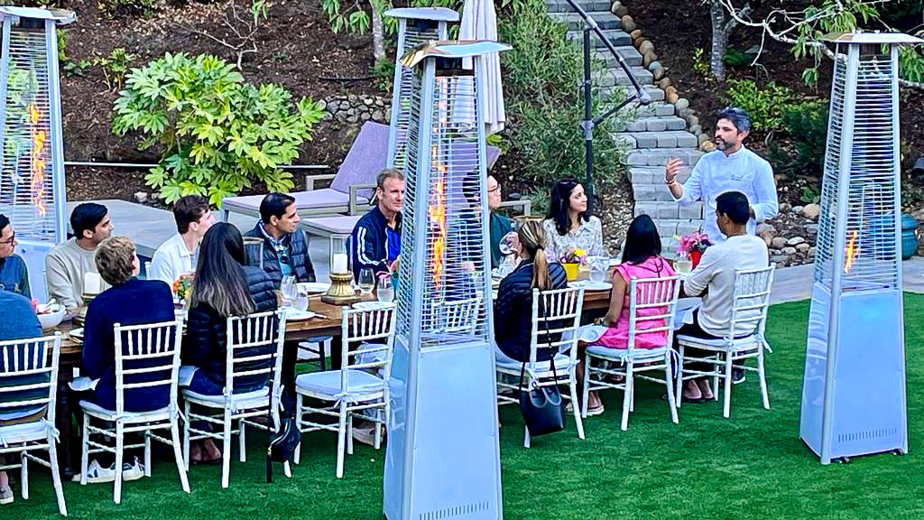 An outdoor dinner party hosted by Chef Olintho, guests seated at a long table under patio heaters