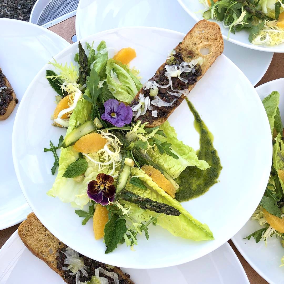A composed salad with citrus, herbs, and grilled bread by Chef Olintho, plated for an outdoor event